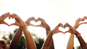 Photo of four pairs of hands stretch upward with hands forming heart shapes.